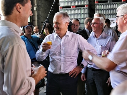 Prime Minister Malcolm Turnbull holds a cup of juice while surrounded by people.