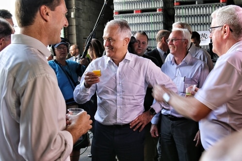 Prime Minister Malcolm Turnbull holds a cup of juice while surrounded by people.