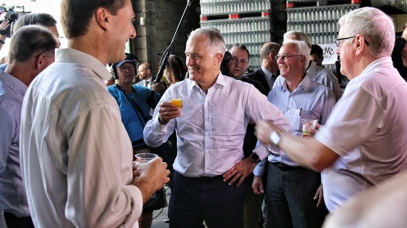 Prime Minister Malcolm Turnbull holds a cup of juice while surrounded by people.