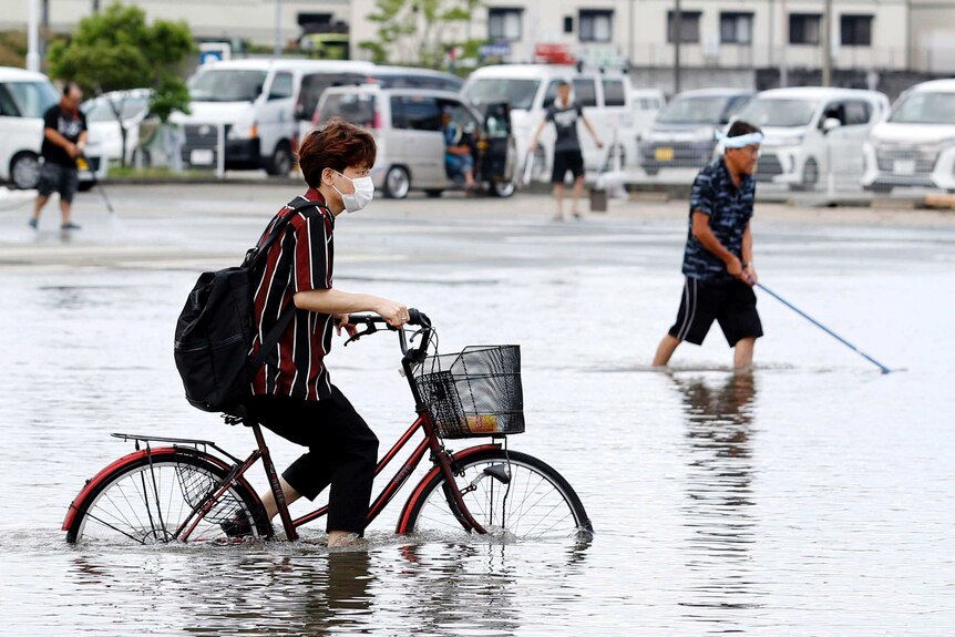 A young man rides a pushbike through brown floodwaters that rise halfway up its wheels.