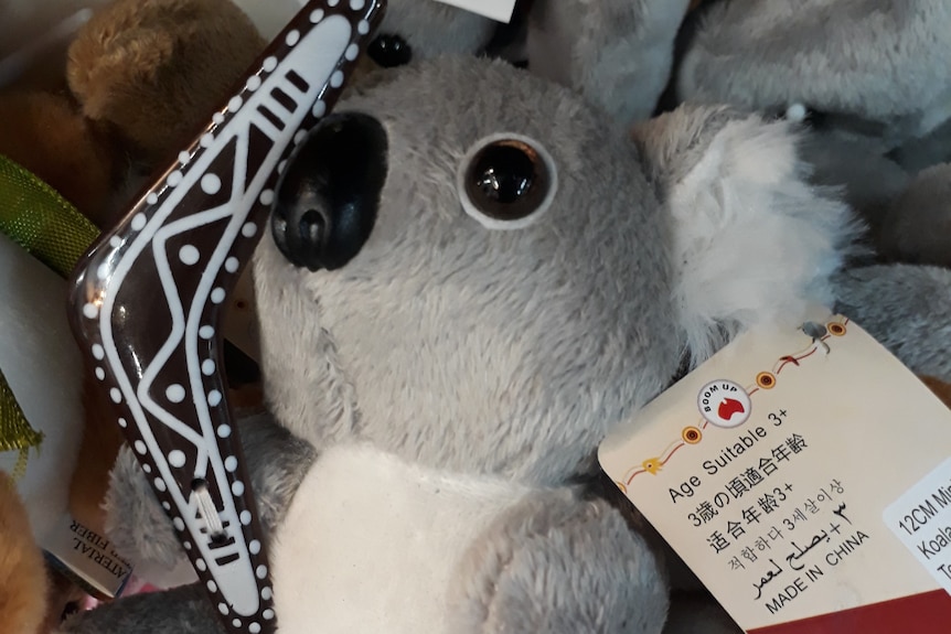 A small stuffed toy koala holding a boomerang with a tag saying "Made in China".
