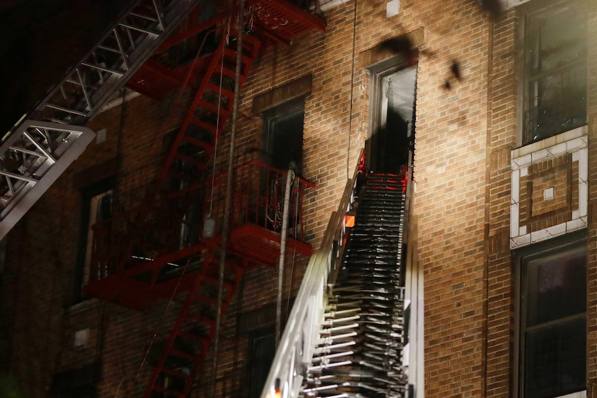 Long ladder reaches up to brick building bathed in flood lights