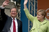 Armin Laschet and German Chancellor Angela Merkel smile and wave to supporters.