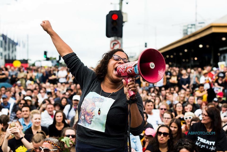 Shareena Clanton speaks on a megaphone as she addresses a crowd of people, some with Aboriginal flags, in Melbourne's CBD.