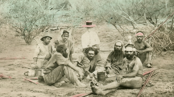 A vintage photograph of people sitting on the ground in the scrub