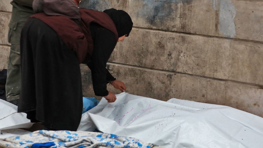 A woman checks a covered body in Aleppo, Syria, one of the victims of the Feb 2023 earthquake