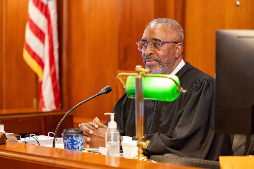 A black man in judges robes at the front of the court. 
