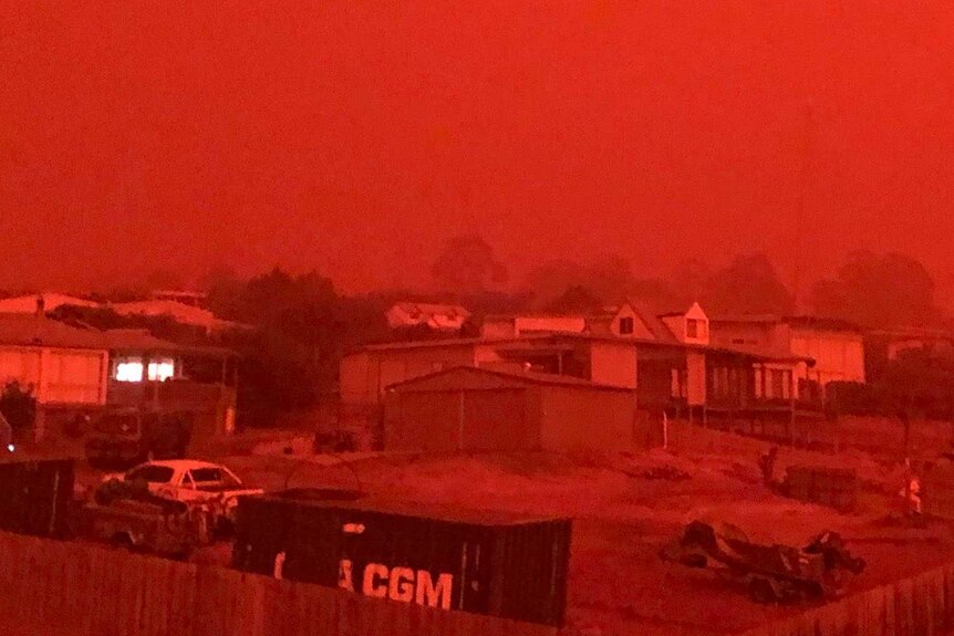 A bright red sky can be seen over houses.