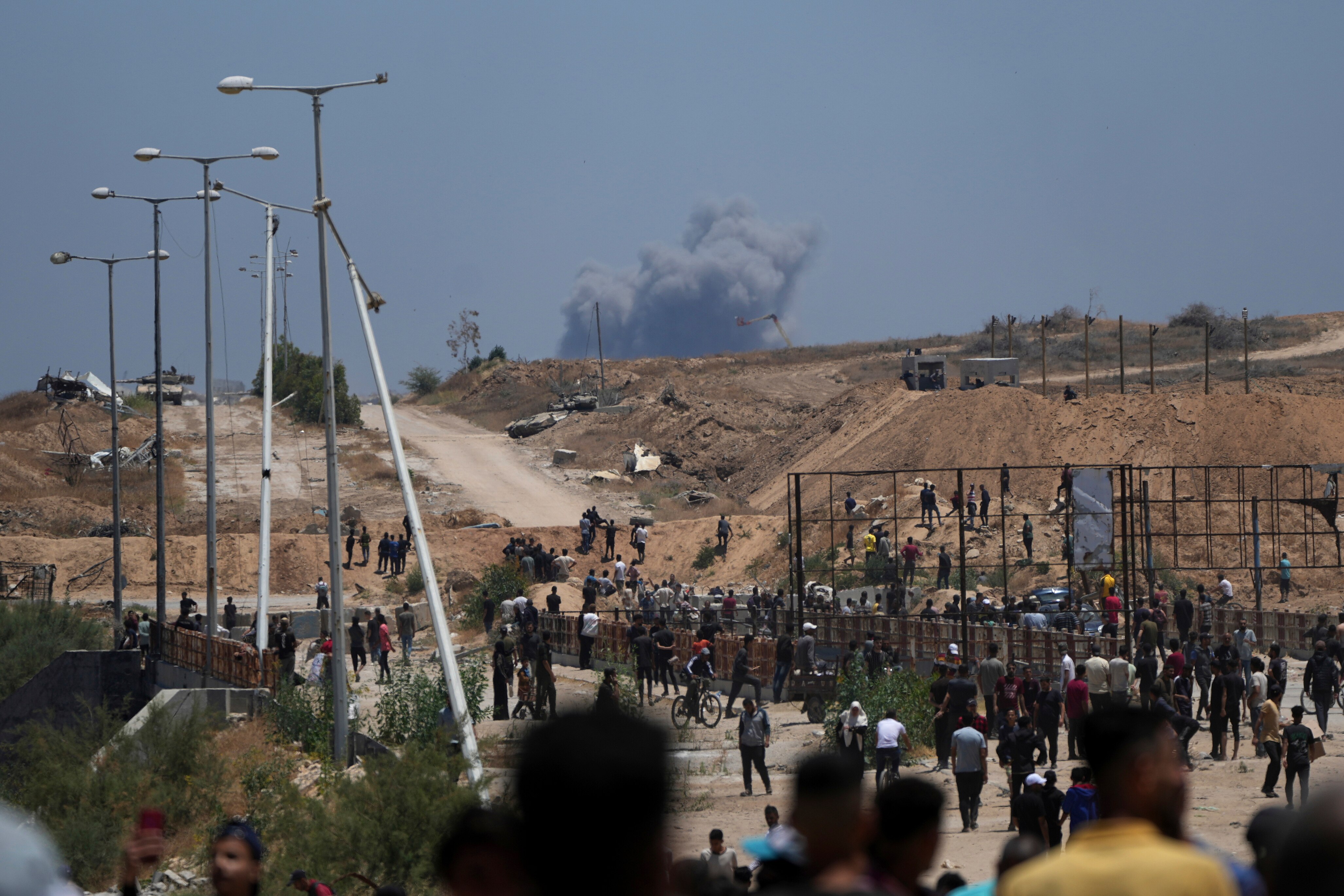 A cloud of smoke rising in the background as people walk on dirt paths