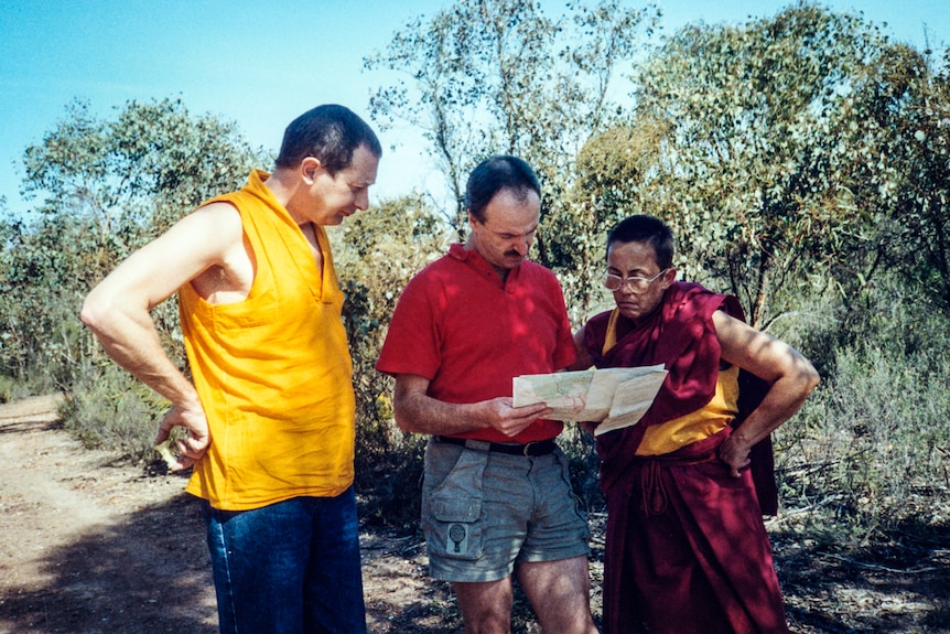 Ian holding a map flanked by two people, one a monk in robes.