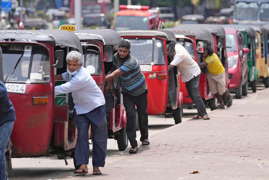 Men pushing their three-wheeled rickshaw taxi vehicles along the street