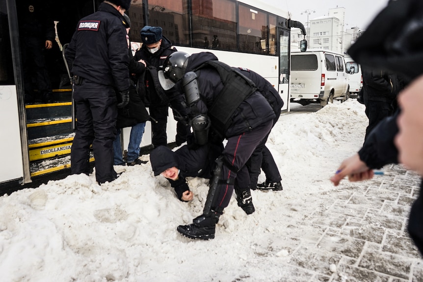 Police arrest a man lying in snow.
