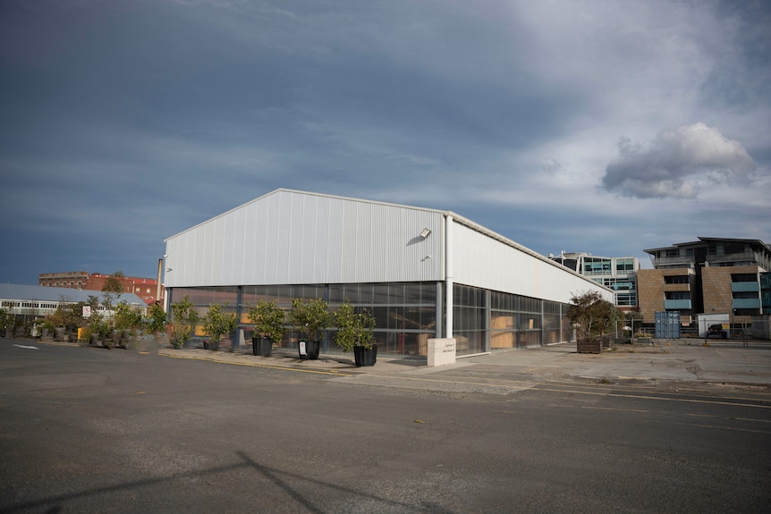 A warehouse in a car park with a corrugated iron top and clear plastic walls on the bottom, surrounded by plants 