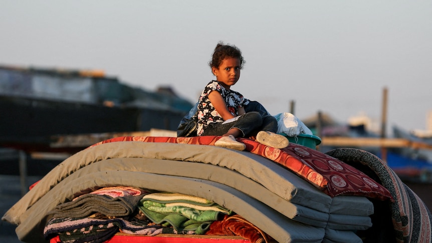 A Palestinian child sits on top of a pile of matresses on a road.