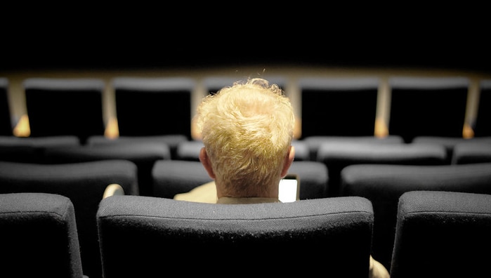 A person shown from the back of the head sits in a cinema