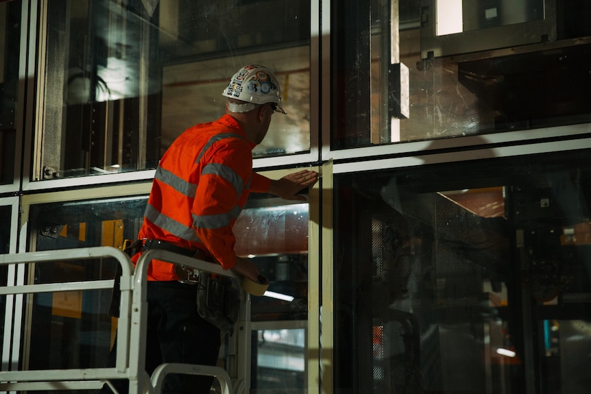 A worker on a lift in high vis and hard hat touching a metal window frame