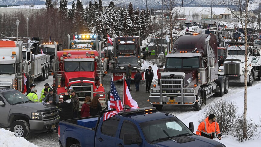 Several trucks stopped alongside a ute with a US and Canadian flag