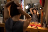 An actor looks into a mirror as she fixes her hair. 