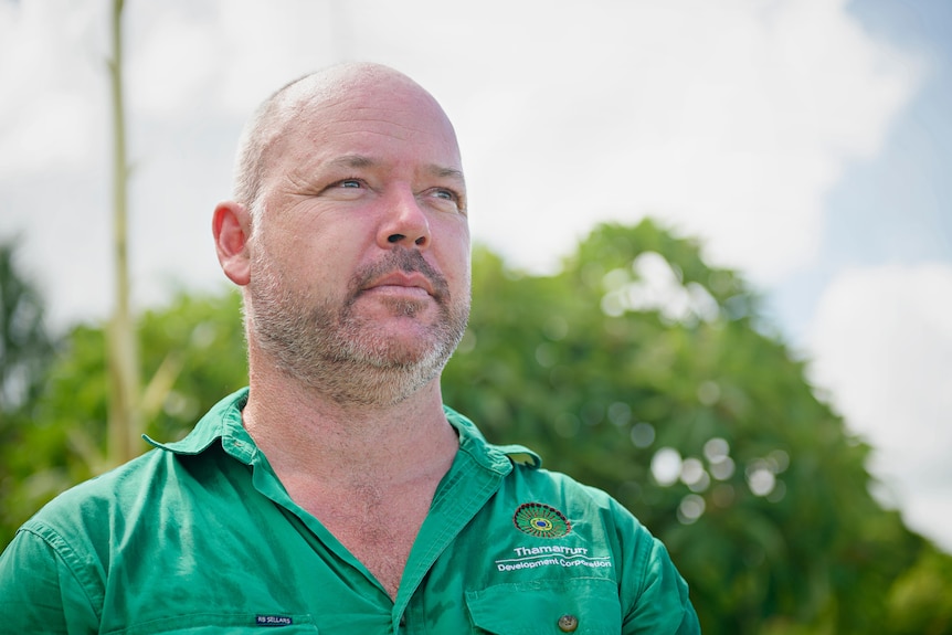 A man wears a green shirt and looks into the distance. 