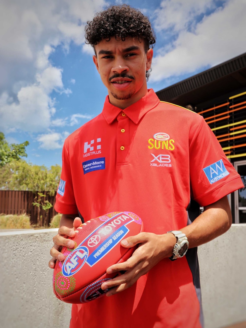 An image of Malcolm Rosas standing holding a football after the announcement he is is a priority pick for the Gold Coast Suns