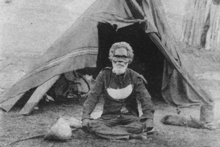 A black and white photo of a grey bearded indigenous man with a 'King Plate' around his neck.