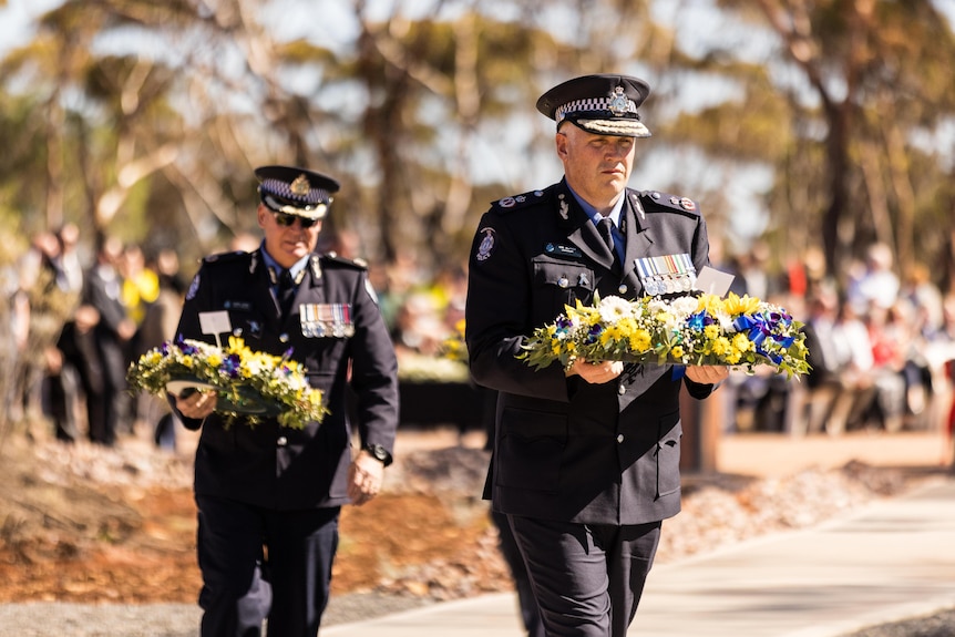 The WA Police Commissioner in uniform carrying a wreath at a memorial service. 