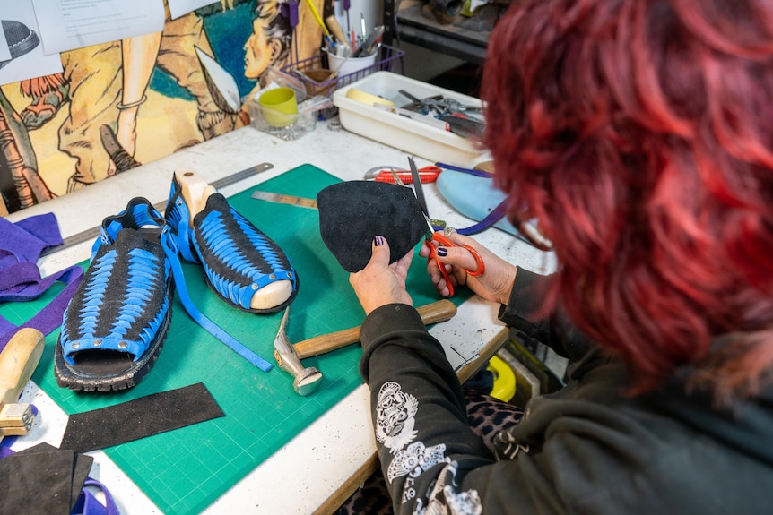 Suede shoes sitting on a workshop bench and a woman cutting suede with scissors.