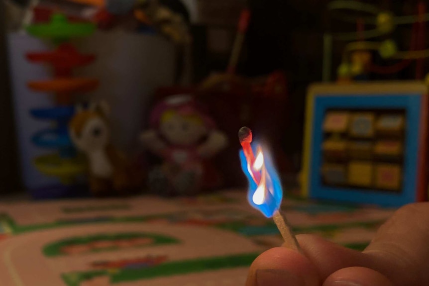 A lit match held with toys in the background