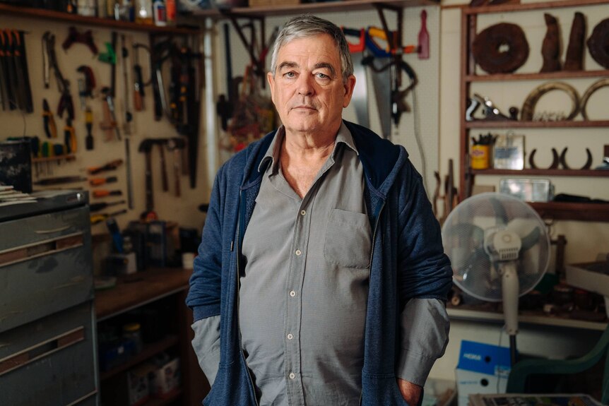A man stands in a workshop that has tools arranged on the walls.