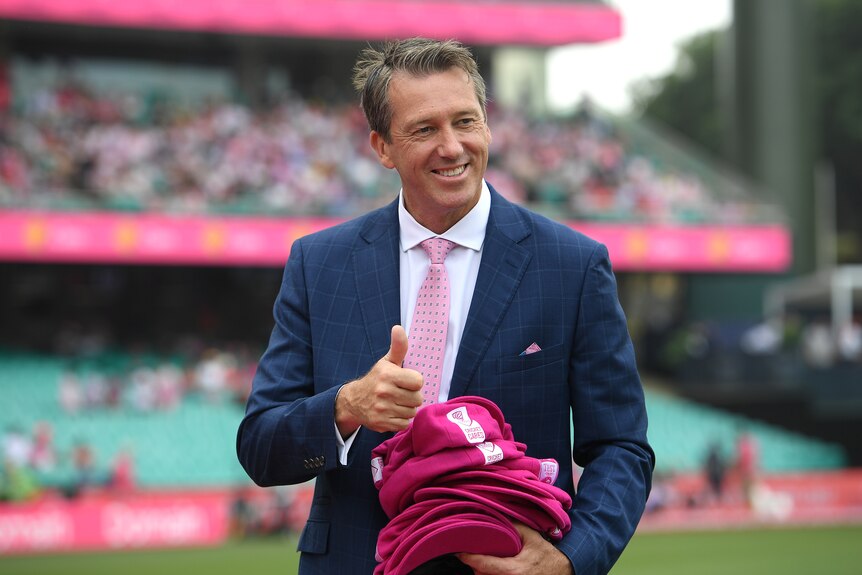 Glenn McGrath gives thumbs up wearing a navy suit and pink tie on the cricket field