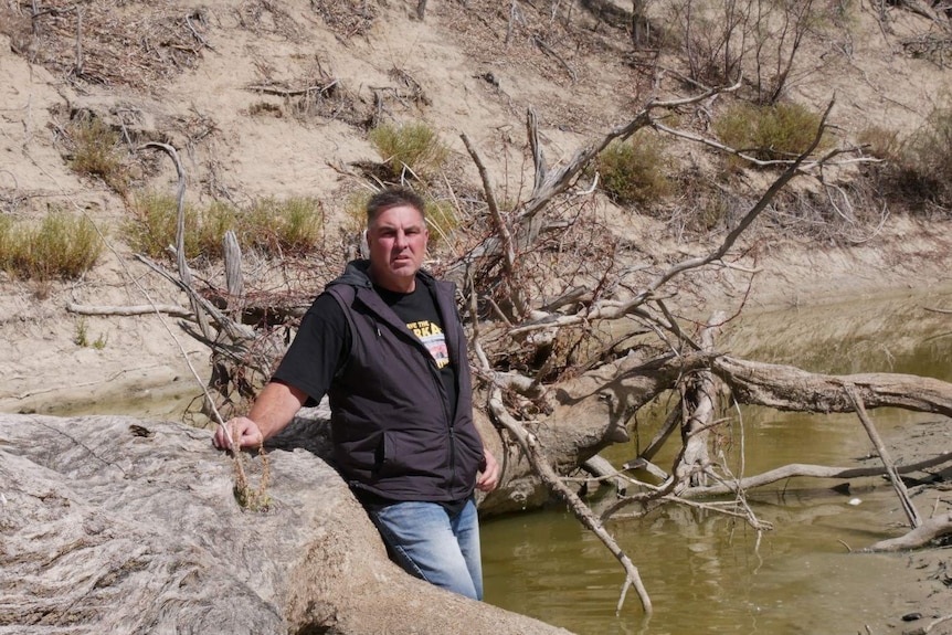 Graeme McCrabb leaning against a tree and standing in a shallow pool of water along the Darling River
