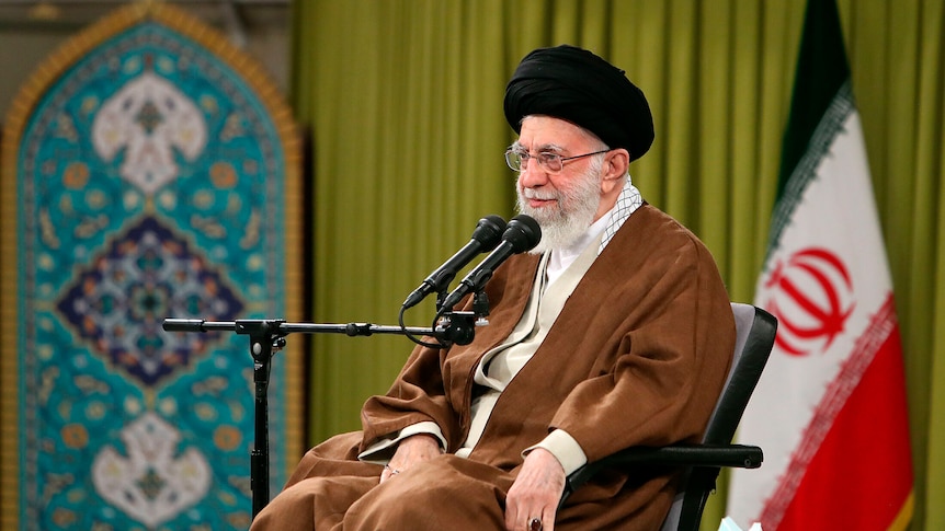 A man sitting in front of a microphone wearing a black turban and brown clothing