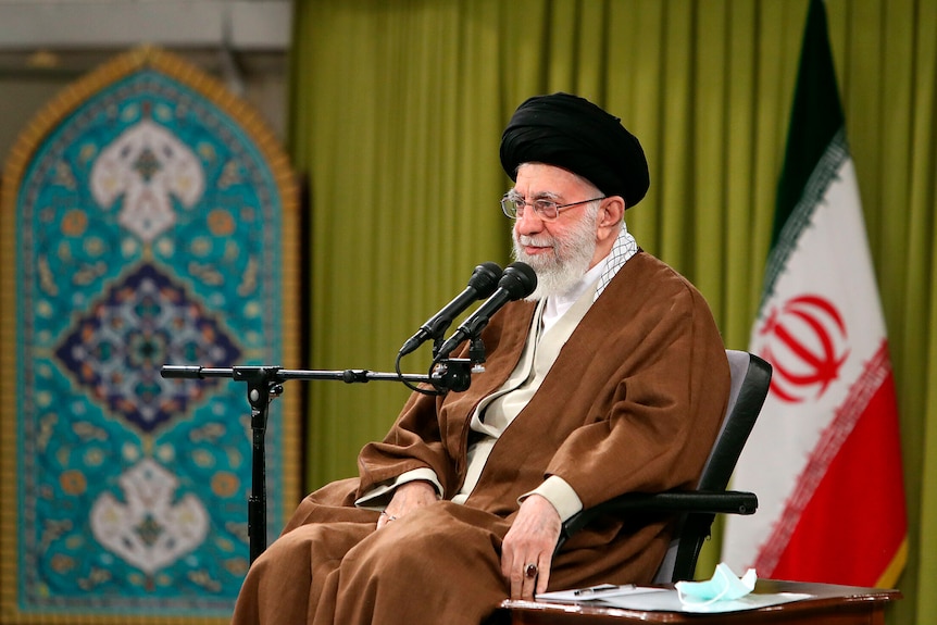 A man sitting in front of a microphone wearing a black turban and brown clothing