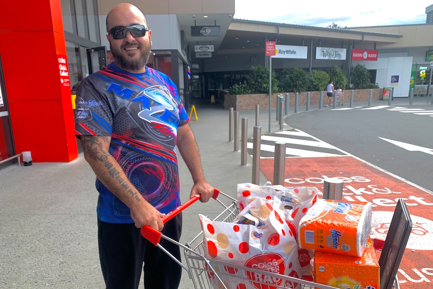 Smiling man in bright colourful shirt with trolley full of shopping.