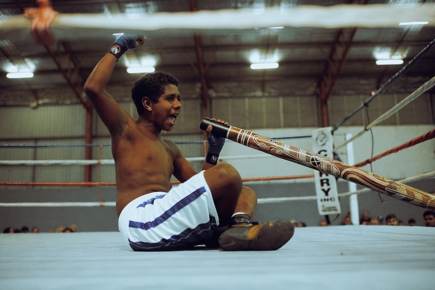 Young boxer Dion plays the digeridoo while sitting on the ring at Derrick's Boxing gym