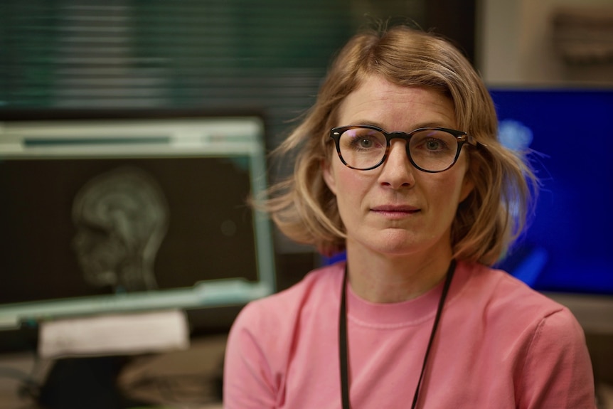 a woman sitting in front of a screen with a brain scan on it