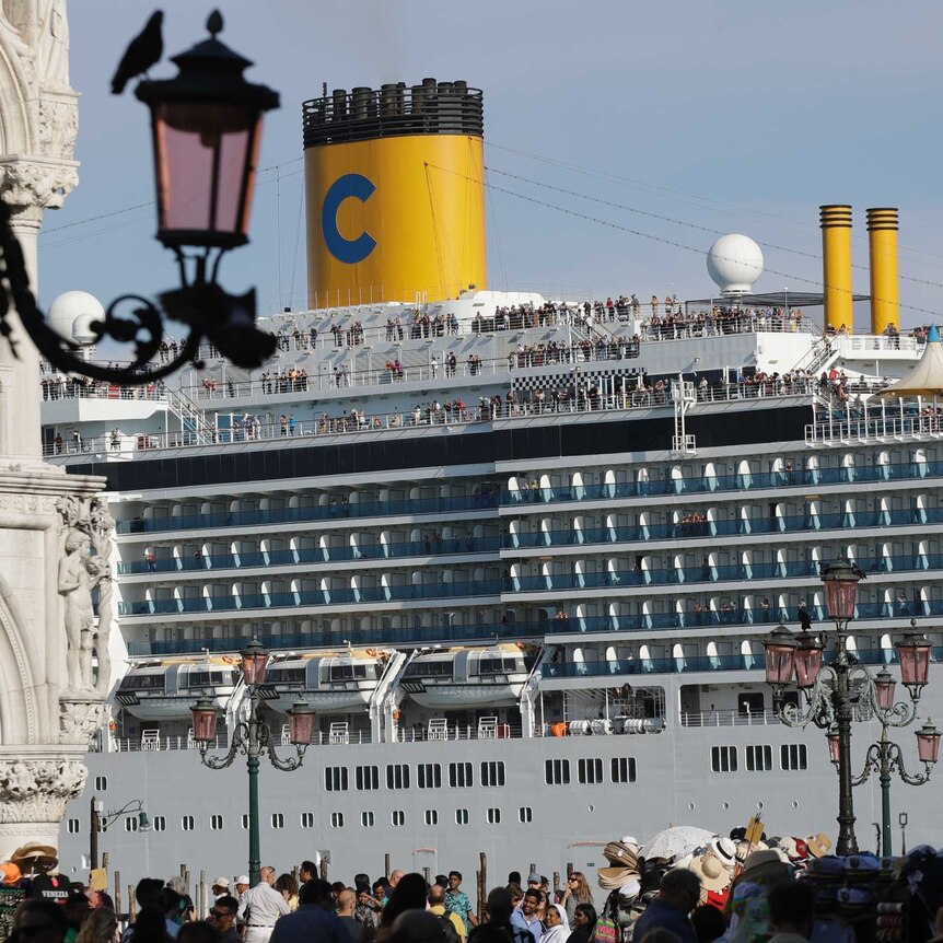 A large cruise ship with yellow funnels sits in Venice lagoon at St Mark's Square in Venice.