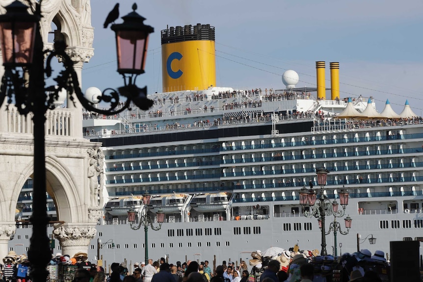 A large cruise ship with yellow funnels sits in Venice lagoon at St Mark's Square in Venice.