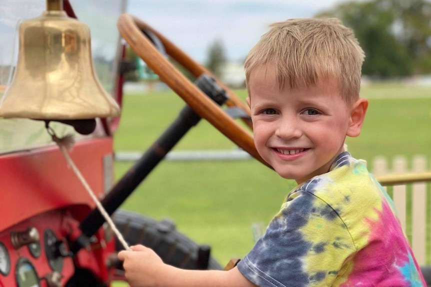 A young boy smiles as he rings a bell on a vintage fire truck.