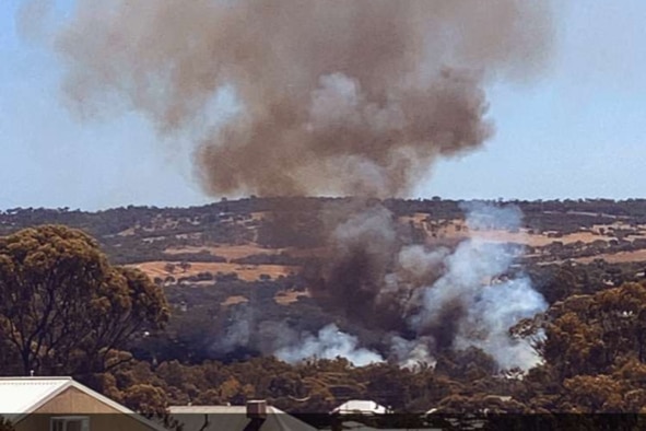 Smoke from a bushfire burning with homes in the foreground and rolling hills in the background