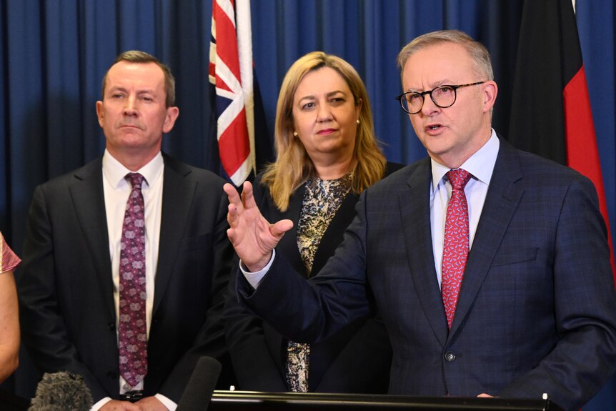 Anthony Albanese gestures as he speaks at a podium with Mark McGowan and Annastacia Palaszczuk standing to his right.