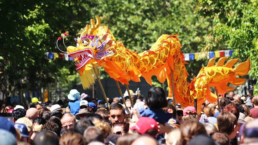 A brightly coloured dragon puppet on sticks weaves above the heads of a crowd.