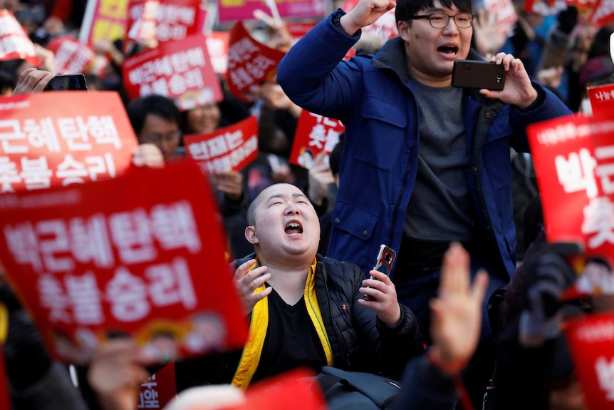 A man on his knees looks up to the sky in happiness at a rally celebrating the impeachment of Park Geun-hye.