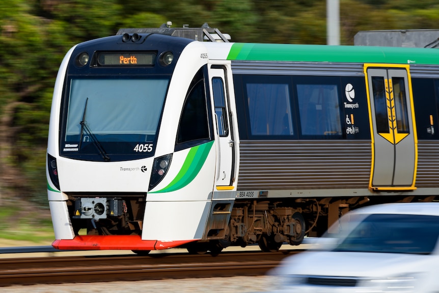 A Transperth passenger train in daylight moving on a railway track near a freeway.