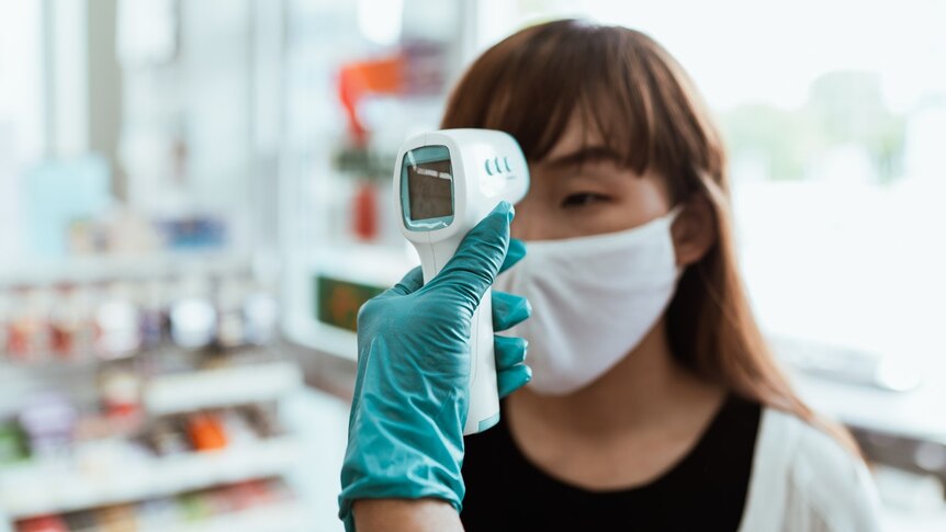 A woman wearing a face mask has her temperature checked