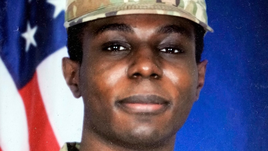 A photo of Travis King in army uniform, standing in front of an American flag. He is a black man  in his 20s with dark eyes.
