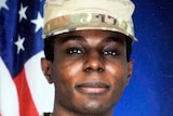 A photo of Travis King in army uniform, standing in front of an American flag. He is a black man  in his 20s with dark eyes.