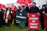 Workers stand holding signs stating 'solidarity' and 'stand up fight back'