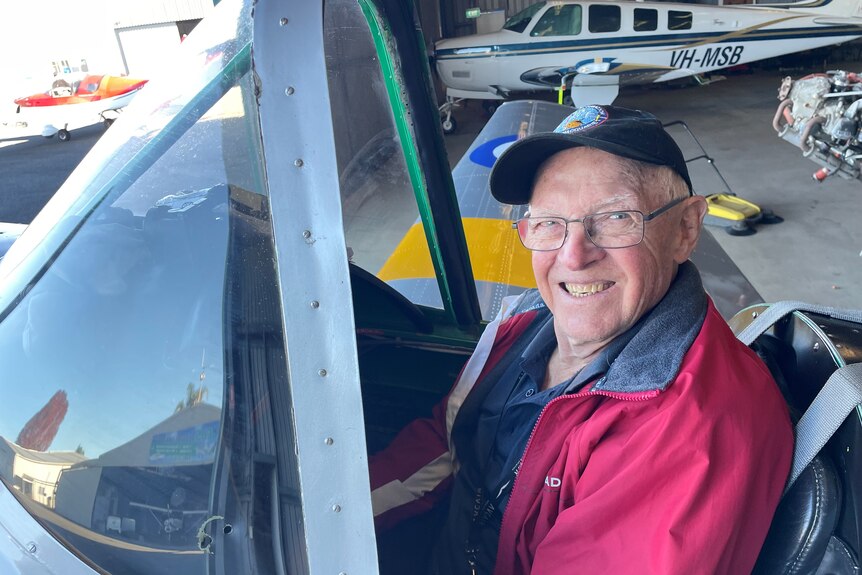 An older man sits inside the cockpit of a small vintage plane, smiling.