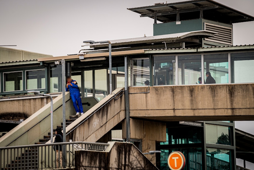 Commuters walk along a pedestrian overpass at a railway station.